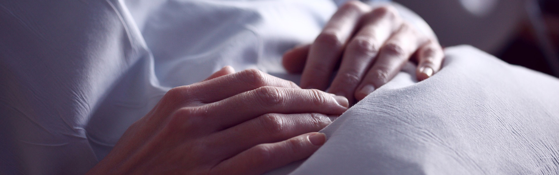 A person's hands are folded on their abdomen as they recline under a sheet.
