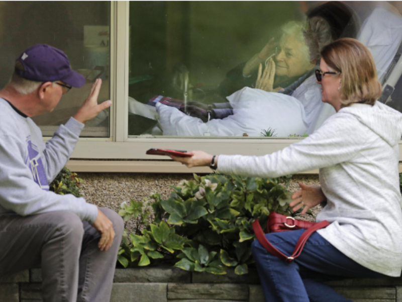 two people outside of a window visiting a patient in a hospital